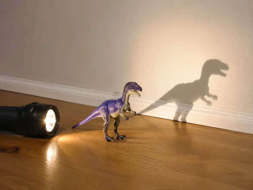 Torch shining on a dinosaur toy to create a shadow on a wall